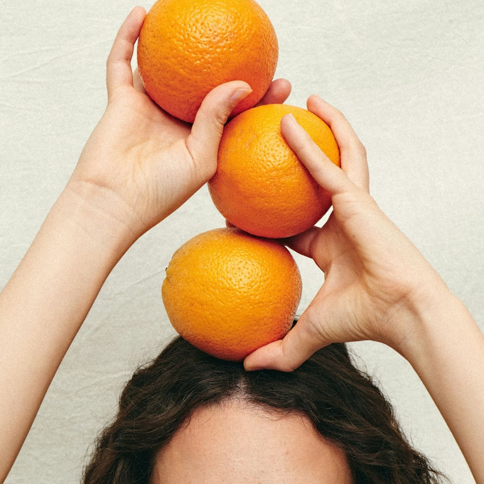 woman with curly hair balancing oranges on her head