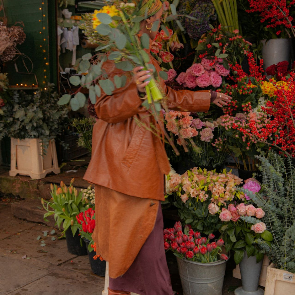 a woman wearing an orange leather jacket  and hijab shopping for flowers for herself