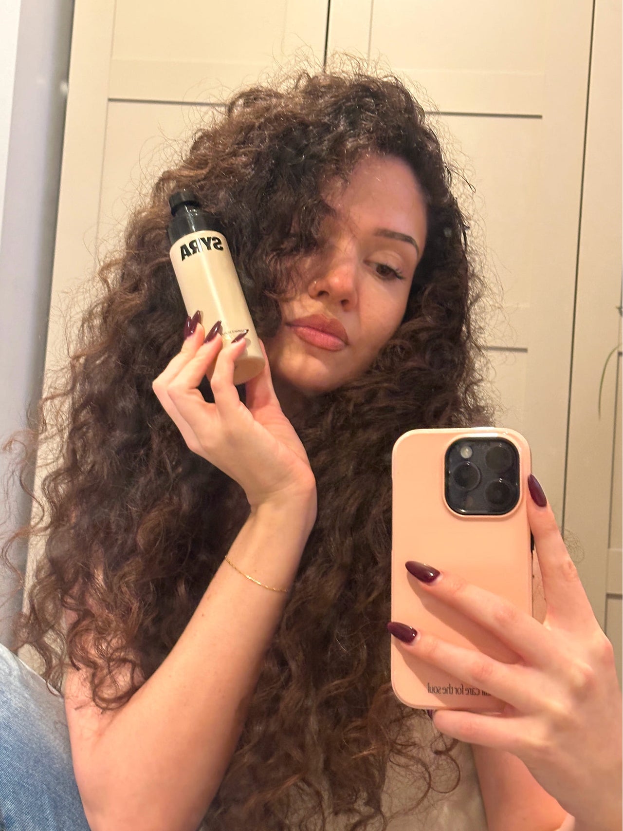 Person holding a Syra bottle labeled in front of their face, taking a mirror selfie.